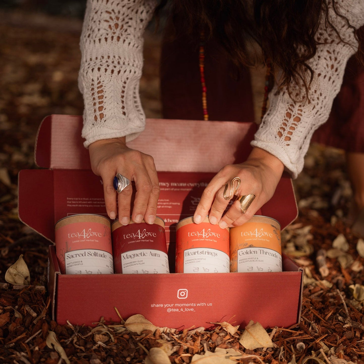 Person holding a box of four cylindrical products with visible branding on a natural background.