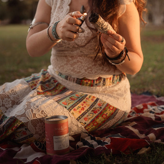 Woman sitting on a blanket outdoors, holding a can and a small object.