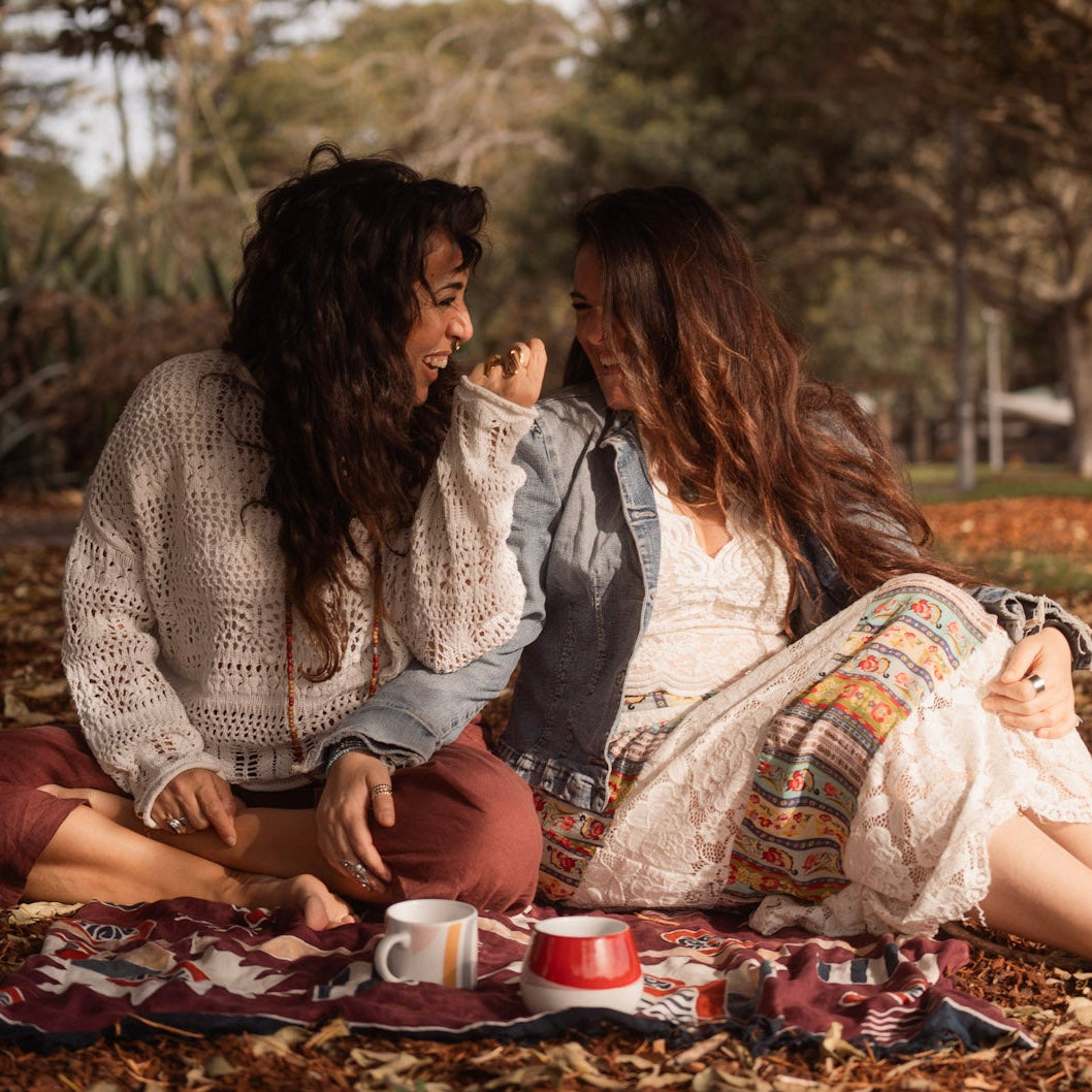 Two people sitting on the ground under a tree, enjoying a picnic.