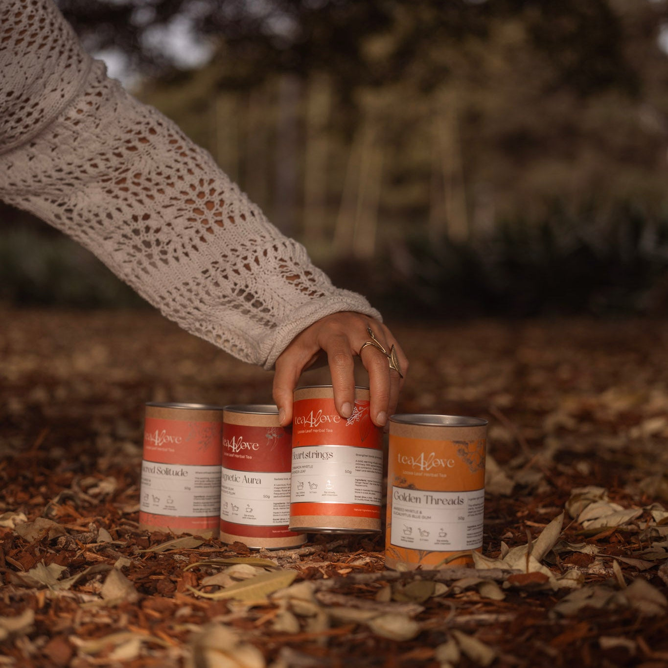 Person reaching for a can among others on a leaf-covered ground with a blurred natural background
