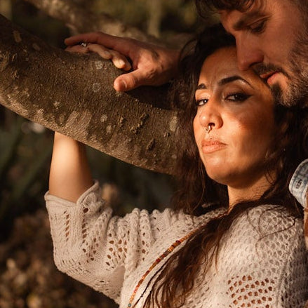 Two people standing close together under a large tree in a natural setting