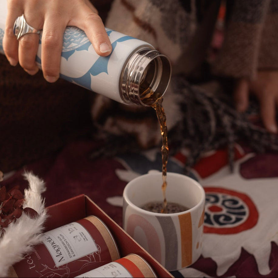Person pouring tea from a thermos into a cup on a patterned blanket.