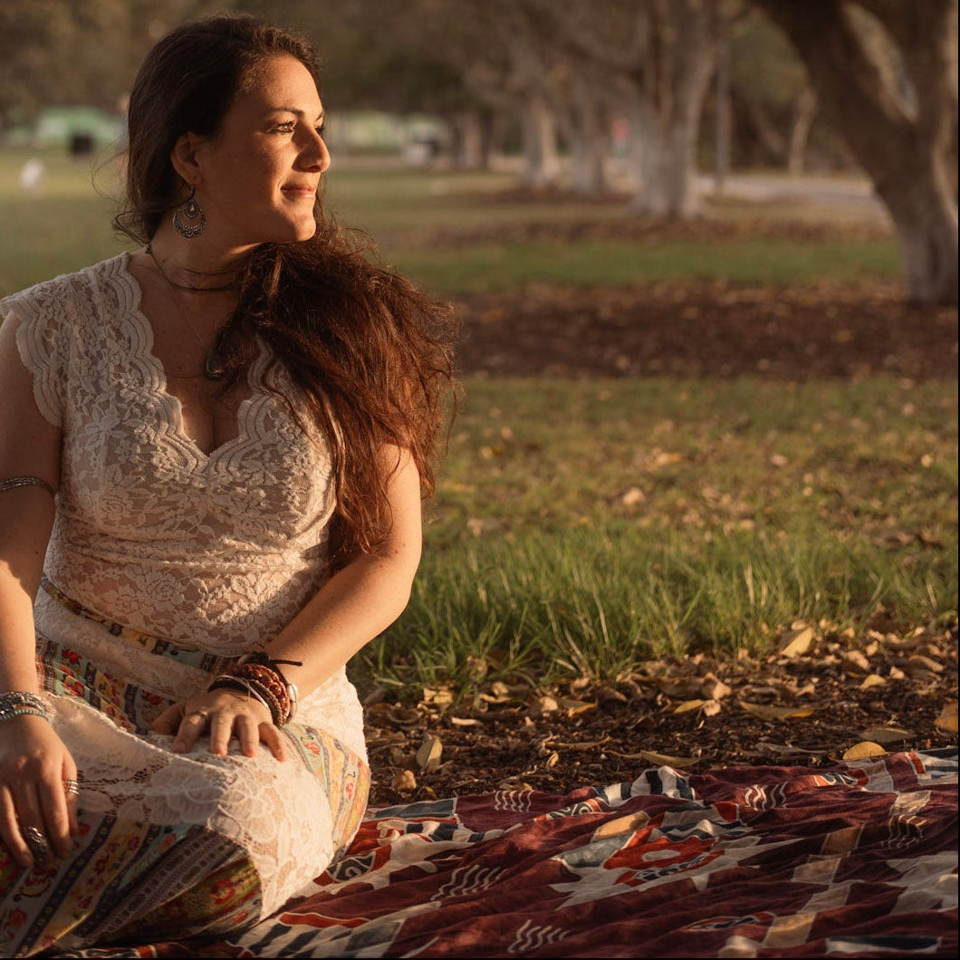 Woman sitting on a blanket in a park with trees and grass in the background