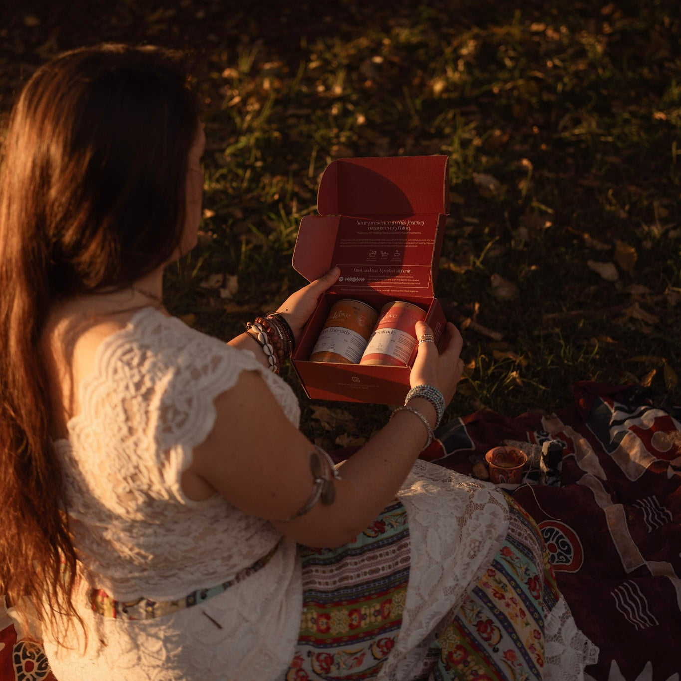 Woman sitting on a blanket in a field, holding a box with items inside.