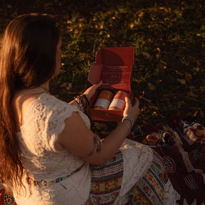 Woman sitting on a blanket in a field, holding a box with items inside.