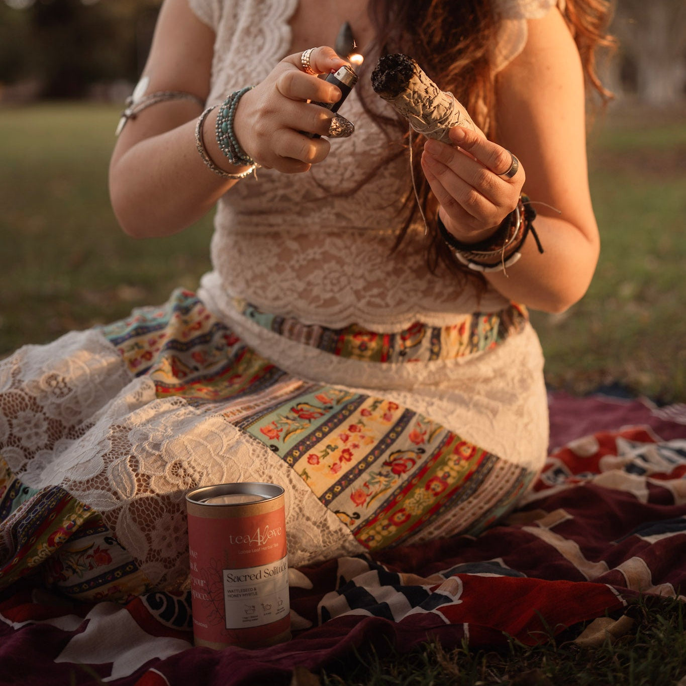 Woman sitting on a blanket outdoors, holding a can and a small object.