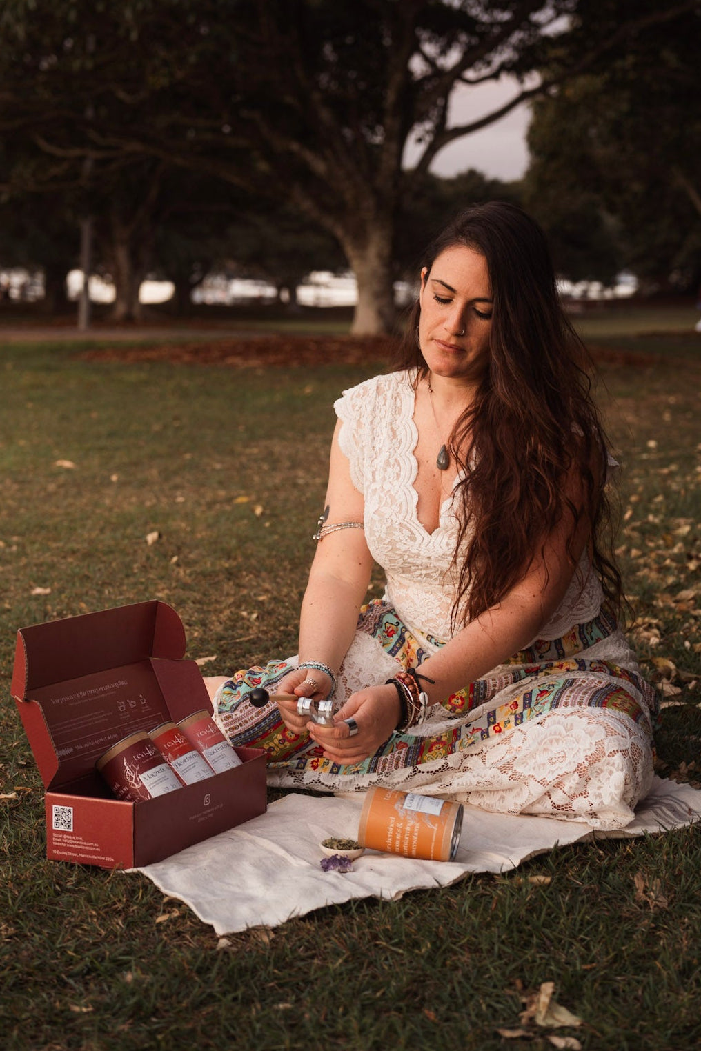 Woman sitting on a blanket in a park, opening a box.